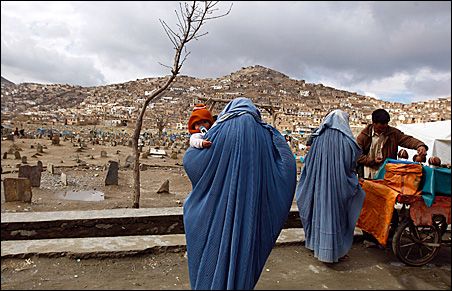 Photo Credit: REUTERS/Ahmad Masood An Afghan woman clad in a burqa holds her child as another woman buys coconut at a cemetery in Kabul earlier this week. A new law for Shiite Muslims has prompted an international uproar.